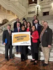 Pennsylvania legislators and the executive director and another director at Pennsylvania Policy Center stand behind a Pennsylvanians Together "For Our Common Wealth" sign in the rotunda of the PA state Capitol building.